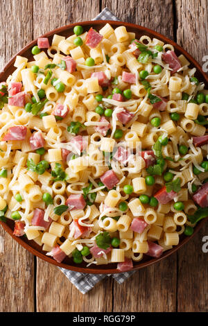 Traditionelle italienische pasta Ditalini mit grünen Erbsen, Schinken und Käse closeup auf einem Schild an einem Holztisch. Senkrechte Draufsicht von oben Stockfoto