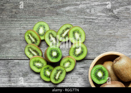 Herzförmige Kiwi mit Kiwi in einer Schüssel auf rustikalen Holzmöbeln Hintergrund. top View Stockfoto