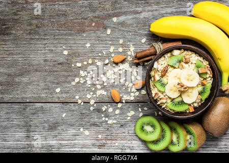 Gesundes Frühstück. hausgemachtem Müsli mit Hafer, Kiwi, Bananen, Nüssen und Zimt in einer Schüssel über rustikal Hintergrund mit Kopie Raum. top View Stockfoto