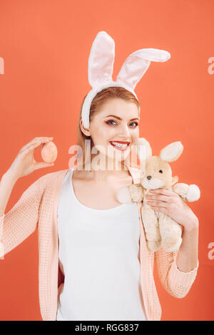 Glückliche Frau im bunny Ohren mit Spielzeug. Frau in Kaninchen bunny Ohren. Frohe Ostern. Frühling Urlaub. Mädchen mit Hase Spielzeug. Ostereiersuche. Osterhase mit Ostereiern Stockfoto