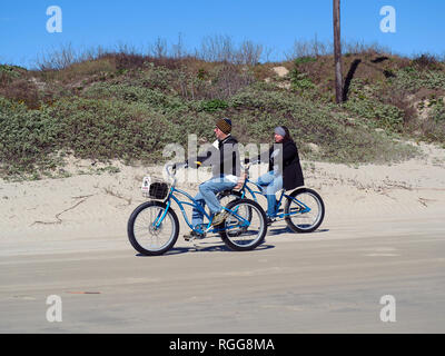 Einen gemütlich gekleideter Mann und Frau fahrt Beach Cruiser style Fahrräder in kühlen Januar Wetter am Strand in Port Aransas, Texas USA. Stockfoto