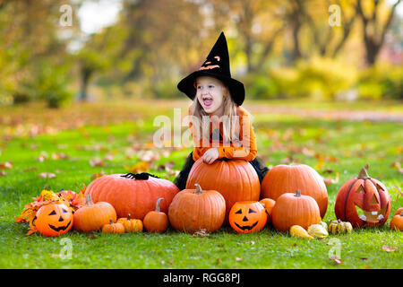 Kinder in schwarz und orange Hexe Kostüm und Hut spielen mit Kürbis und Spinne im Herbst Park auf Halloween. Kinder Trick oder Festlichkeit. Kleines Mädchen Carving Stockfoto