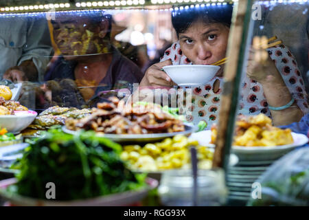 Frau suchen an der Kamera beim Essen Essen mit Stäbchen auf einem Markt in Hoi An, Vietnam, Asien Stockfoto