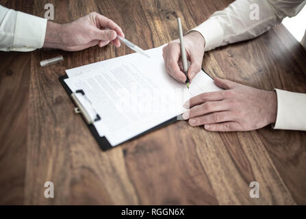 Man unterzeichnen Vertrag an den hölzernen Schreibtisch mit anderen Person zeigen auf Dokument Stockfoto