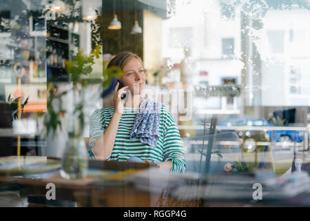 Lächelnde junge Frau auf Handy in ein Cafe Stockfoto