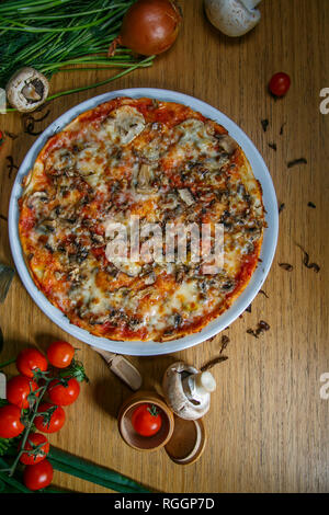 Köstliche italienische vegetarische Pizza mit Tomaten, Pilzen, Paprika, Mais und schwarzen Oliven - dünne Gebäck Kruste an den hölzernen Tisch Hintergrund Stockfoto