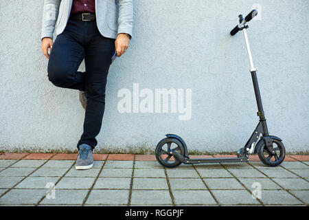 Untere Partie der Geschäftsmann mit Scooter und Handy gegen eine Wand gelehnt Stockfoto