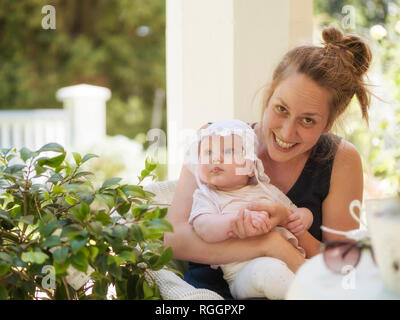 Portrait von lächelnden Mutter mit Baby auf dem Schoß sitzen auf der Terrasse Stockfoto