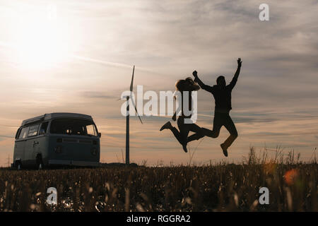 Ausgelassene Ehepaar am Wohnmobil in ländlichen Landschaft bei Dämmerung springen Stockfoto