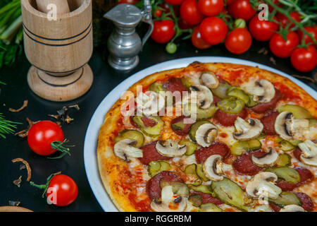 Pizza mit Schinken, Salami, Gurken, Oliven, Ananas, Tomaten, Paprika, Käse, Pilze. Pizza auf einem weißen Hintergrund. Fast food. Schön und kitschig Stockfoto