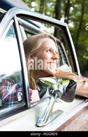 Glückliche junge Frau im Auto im Wald Stockfoto