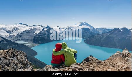 Blick vom Panorama Ridge Trail, zwei Wanderer auf einem Stein saß mit Garibaldi Lake, türkisfarbene Gletschersee, Guard Berg und Stockfoto