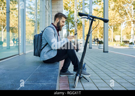 Unternehmer Sitzen im Freien mit Handy neben Scooter Stockfoto