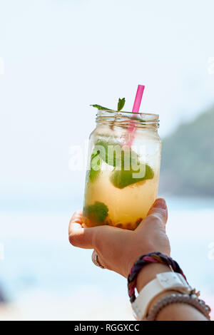 Passion Fruit Mint Mojito Cocktail in der Frau die Hand. Maracuja gefroren Limonade auf Ozean Hintergrund vertikale Ansicht. Sommer frisches Vitamin kaltes Soda Smoothie Stockfoto