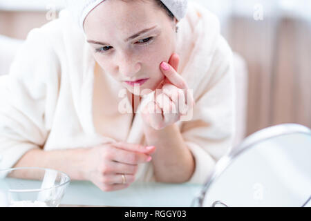Schöne glückliche junge Frau mit einem Handtuch auf dem Kopf an ihrer Haut in einem Spiegel zu betrachten. Das Konzept der rechtzeitige Hygiene und Pflege für die Haut zu Hause Stockfoto