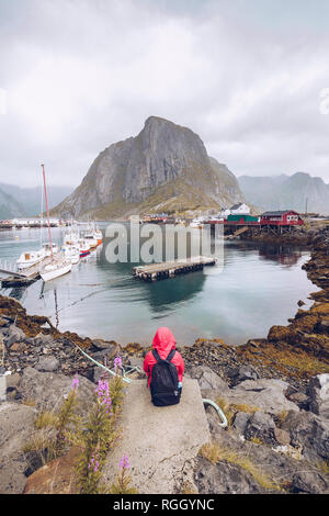 Norwegen, Lofoten, Hamnoy, Rückansicht des Menschen das Tragen der roten Regenjacke und Rucksack in Aussicht Stockfoto