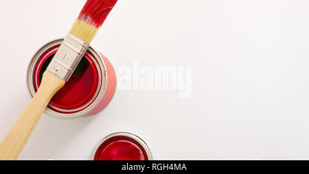 Rote Acrylfarbe Kanister auf weißen Tisch und Pinsel auf Topf öffnen. Konzeptueller Hintergrund der Malerei Material mit Platz für Text. Horizontale compo Stockfoto