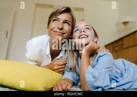 Glückliche Mutter und Tochter auf dem Boden liegend zu Hause beobachten etwas Stockfoto