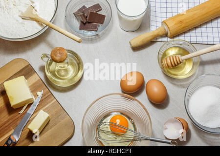 Zutaten für Kuchen backen. Eier, Mehl, Butter, Öl, Milch, Honig, Zucker und Schokolade auf hellen Hintergrund. Backen Konzept, Blick von der hohen Winkel. Stockfoto