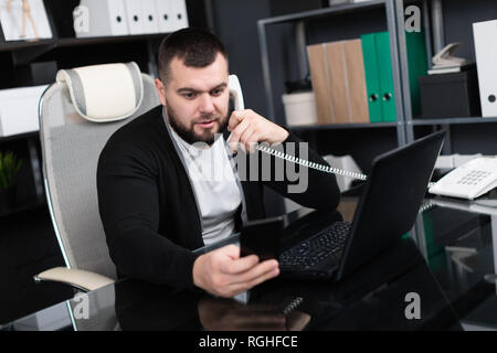 Business Mann bei der Arbeit am Tisch im modernen Büro. Geschäftsmann antworten Telefon beim Sitzen am Computer Schreibtisch im Büro. junger Mann Probleme löst auf Compu Stockfoto