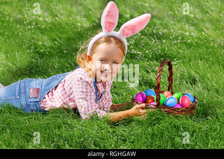 Süße kleine Mädchen mit Korb auf grünem Gras im Park. Easter Egg Hunting Konzept Stockfoto