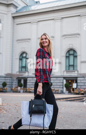 Portrait von lächelnden jungen Frau mit Handtasche und Shopping Bag entlang Stockfoto