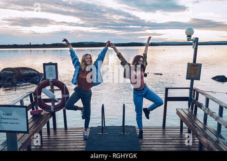 Zwei Freundinnen Stehen auf einem Bein auf einem Pier am See Inari, Finnland Stockfoto