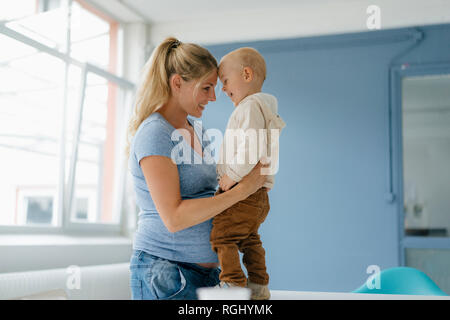 Gerne schwangere Mutter umarmt Toddlersohn stehend auf Tabelle Stockfoto