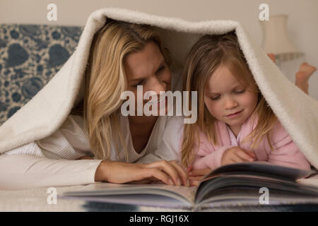 Vorderansicht der glücklichen Mutter mit ihrer jungen Tochter lesen Storybook unter Decke im Schlafzimmer zu Hause Stockfoto