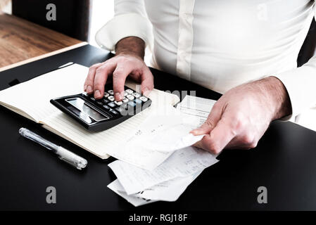 Mann an Schreibtisch mit Rechner, Wechsel oder Kaufbelege und Notpad Stockfoto