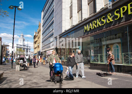 Sheffield, Großbritannien - 26 April 2015: zwei Männer und eine Mutter schieben Kinderwagen vorbei ein strassenmusikant außerhalb M&S Fargate Stockfoto