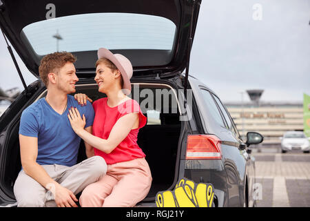 Glückliches junges Paar im Kofferraum am Flughafen sitzen Stockfoto