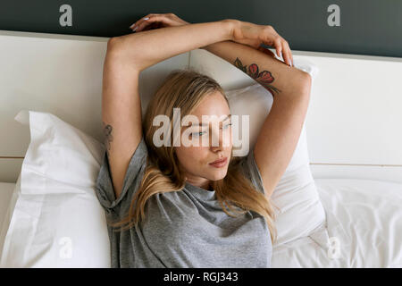 Ernsthafte blonde junge Frau im Bett lag, Stockfoto