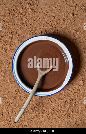 Geschmolzene Schokolade und Löffel aus Holz in eine Schüssel von Kakaopulver umgeben Stockfoto