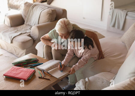 Seitenansicht eines Großmutter ihrer Enkelin helfen bei Hausaufgaben im Wohnzimmer zu Hause Stockfoto