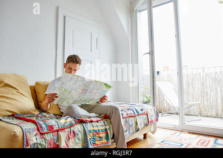 Junger Mann saß auf der Couch zu Hause Lesen der Karte Stockfoto