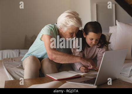 Vorderansicht eines Großmutter ihrer Enkelin helfen bei Hausaufgaben im Wohnzimmer zu Hause Stockfoto