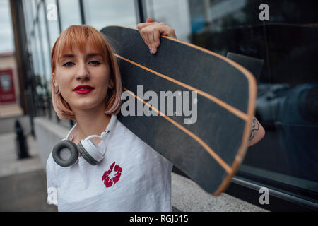 Portrait von selbstbewussten jungen Frau mit Carver skateboard außerhalb eines Gebäudes Stockfoto