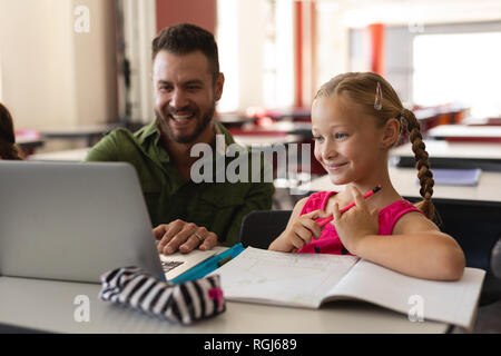 Vorderansicht der jungen Lehrer helfen Mädchen mit Studie über Laptop im Klassenzimmer Stockfoto