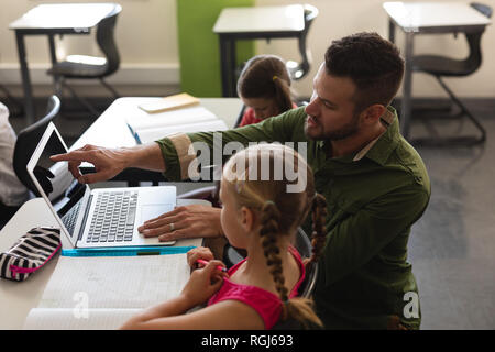 Seitenansicht der jungen Lehrer helfen Mädchen mit Studie über Laptop im Klassenzimmer Stockfoto