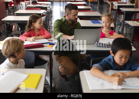 Vorderansicht der jungen Lehrer helfen Mädchen mit Studie über Laptop im Klassenzimmer Stockfoto