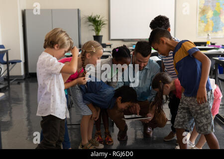 Vorderansicht eines männlichen Lehrer unterrichten Kinder auf digitale Tablette im Klassenzimmer der Volksschule Stockfoto