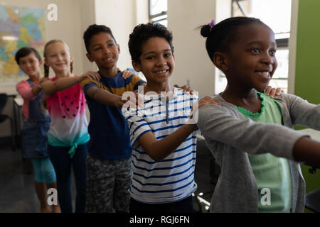 Seitenansicht von Schulkindern in Reihe stehen mit der Hand auf der Schulter im Klassenzimmer Stockfoto