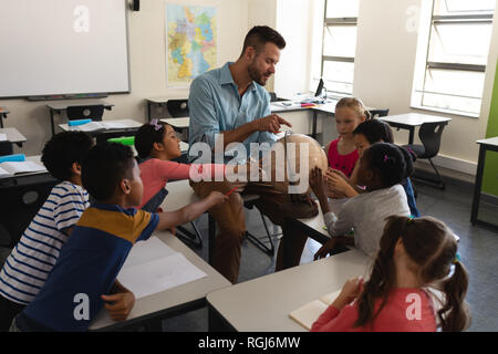 Männliche Lehrer Lehre seine Kinder über Geographie durch die Verwendung von Globe im Klassenzimmer der Volksschule Stockfoto