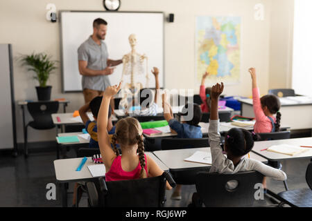 Ansicht der Rückseite des Schule Kinder anheben und Sitzen am Schreibtisch in der Grundschule Stockfoto