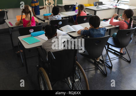 Ansicht der Rückseite des deaktivieren Schuljunge mit Mitschüler studieren und Sitzen am Schreibtisch im Klassenzimmer der Volksschule Stockfoto