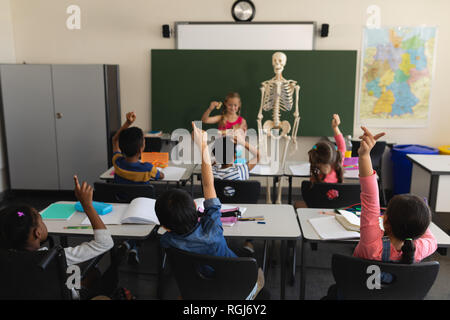 Ansicht der Rückseite des schoolkids heben die Hände und Sitzen am Schreibtisch im Klassenzimmer der Volksschule Stockfoto