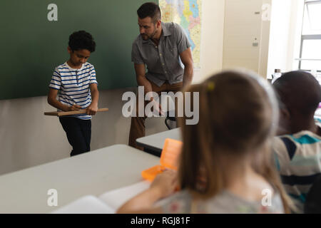 Schüler schreiben auf Schiefer und Lehrer an Ihn im Klassenzimmer der Volksschule Stockfoto