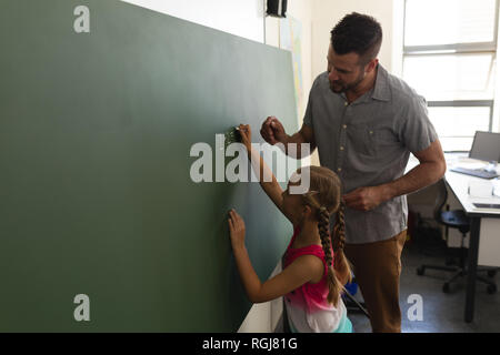 Seitenansicht der Schülerin mit Mathe Lehrer schreiben auf Kreidetafel im Klassenzimmer Stockfoto