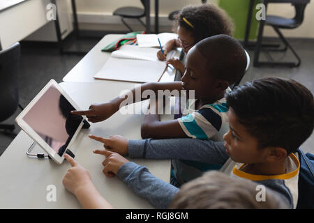 Hohe Betrachtungswinkel von Neugierig schoolkids Studieren auf digitalen Tablet beim Sitzen am Schreibtisch im Klassenzimmer der Volksschule Stockfoto